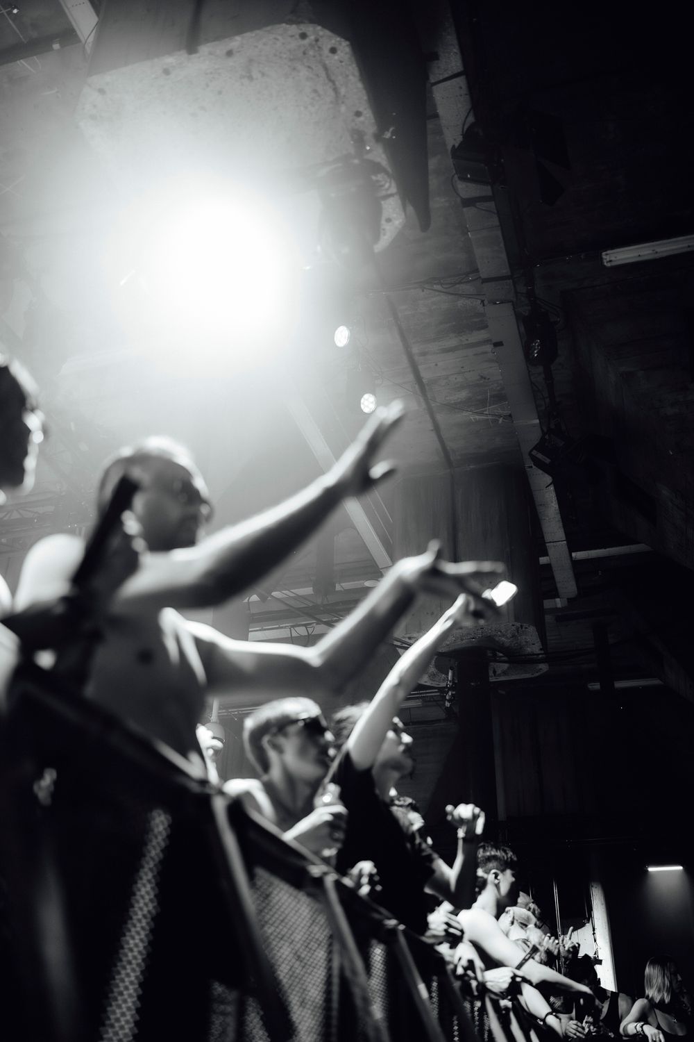 Black and white concert photo showing energetic crowd with arms raised under spotlight.