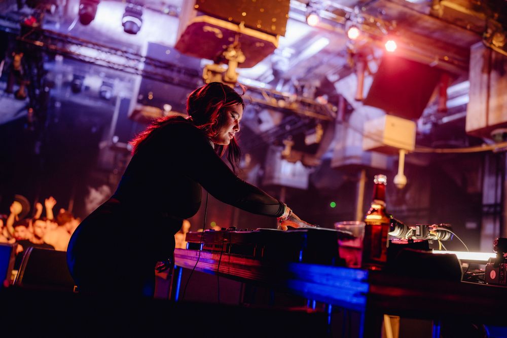 DJ performing on stage with equipment under dramatic lighting at a nightclub event.