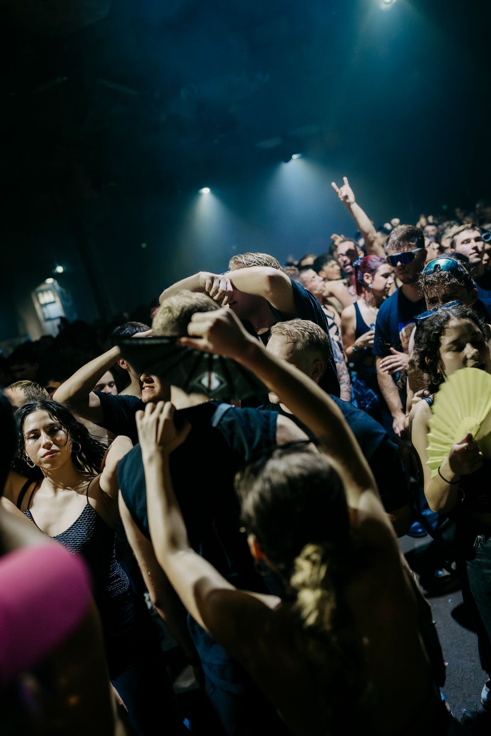 Energetic crowd with raised hands at a music event under dramatic spotlights.