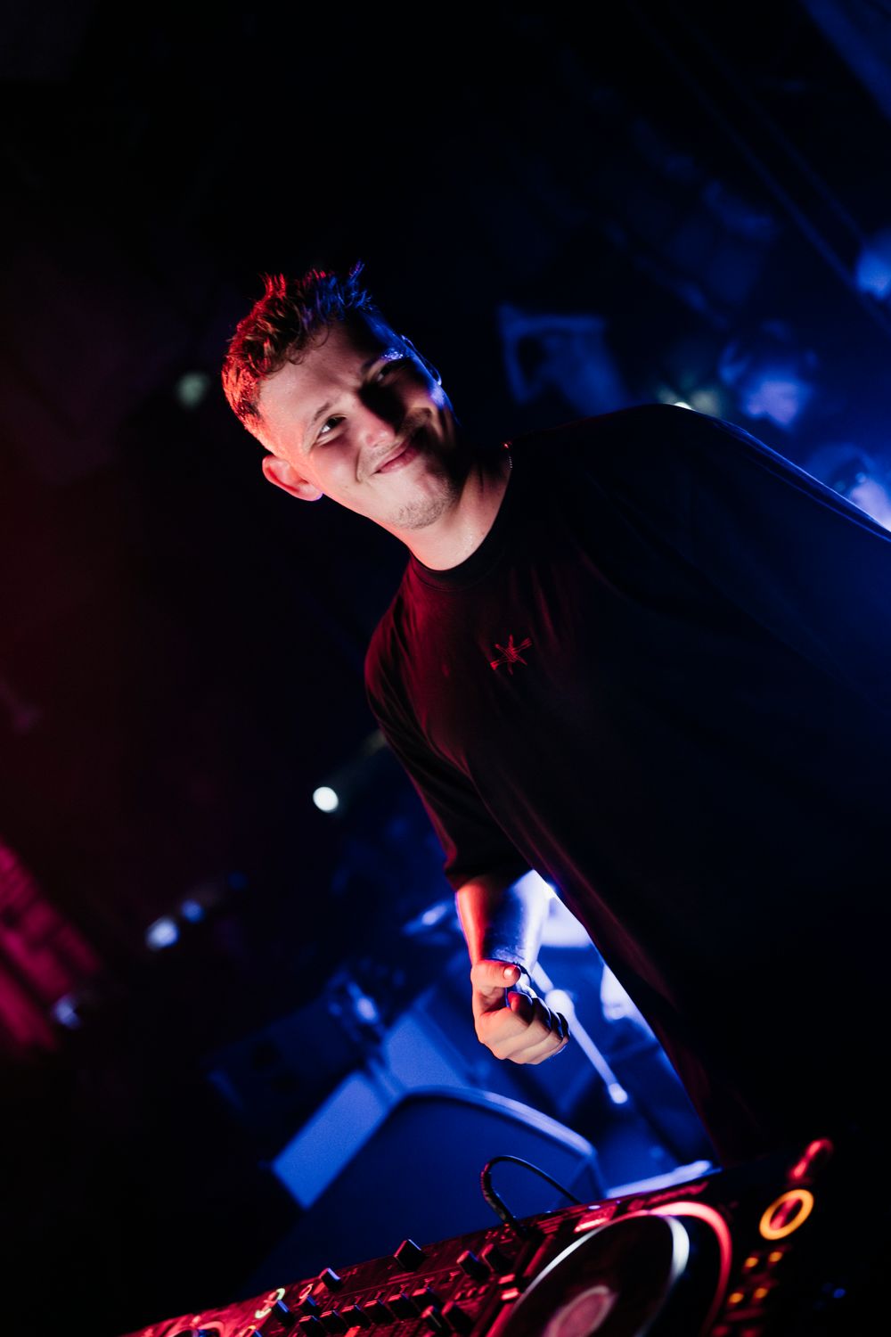 A DJ performs at a nightclub with dramatic blue lighting and entertainment equipment.