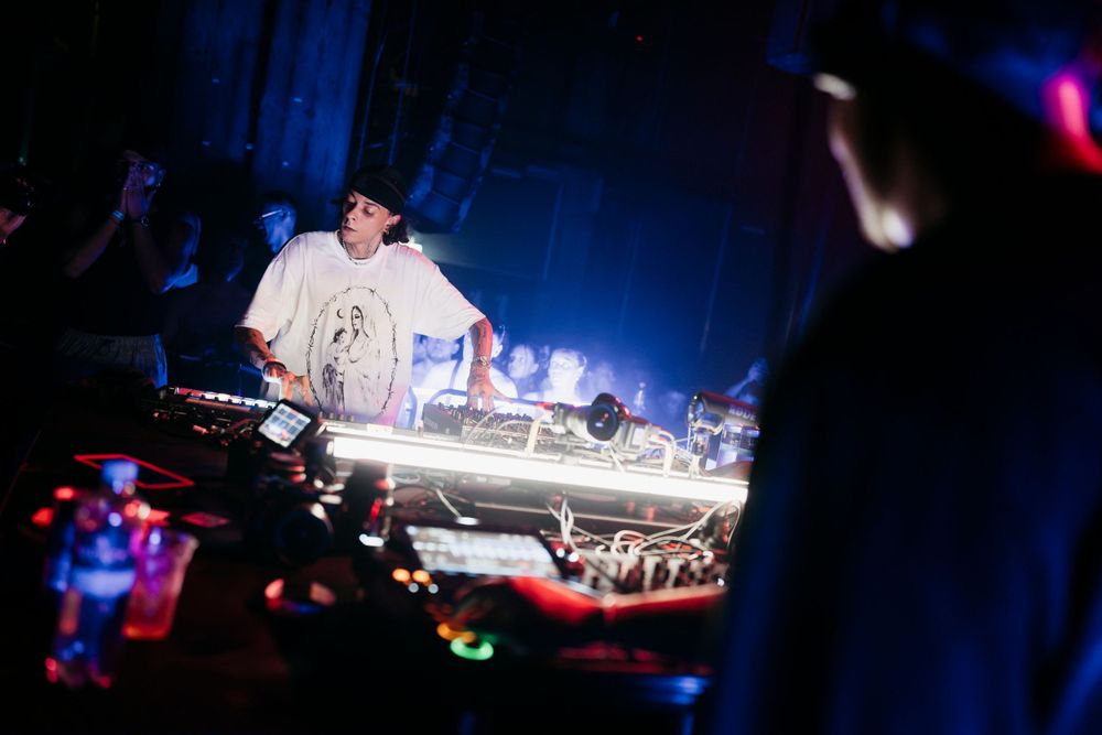 Club DJ performing behind turntables with blue and red atmospheric lighting effects.