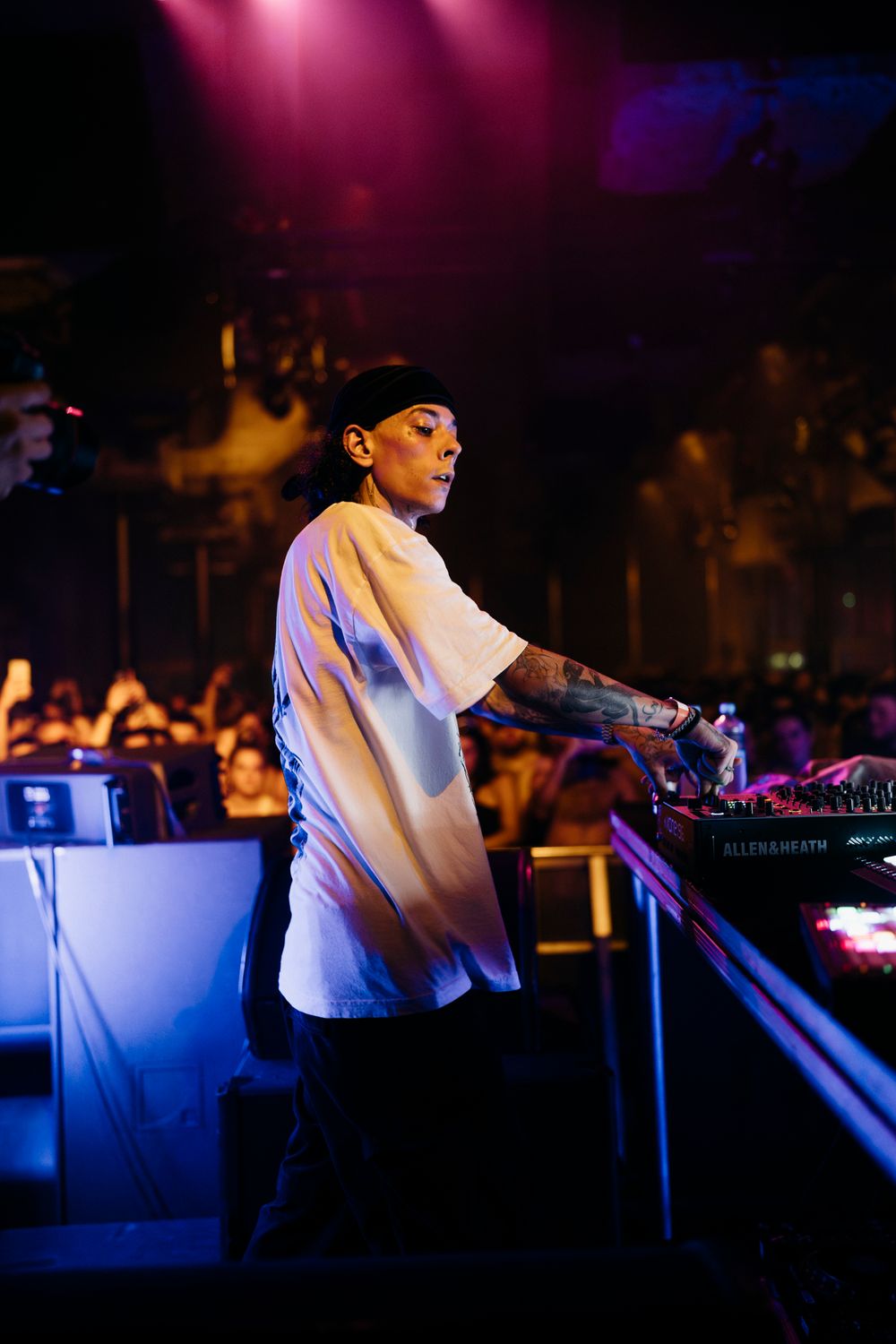 DJ performing with electronic equipment under purple and blue stage lighting.