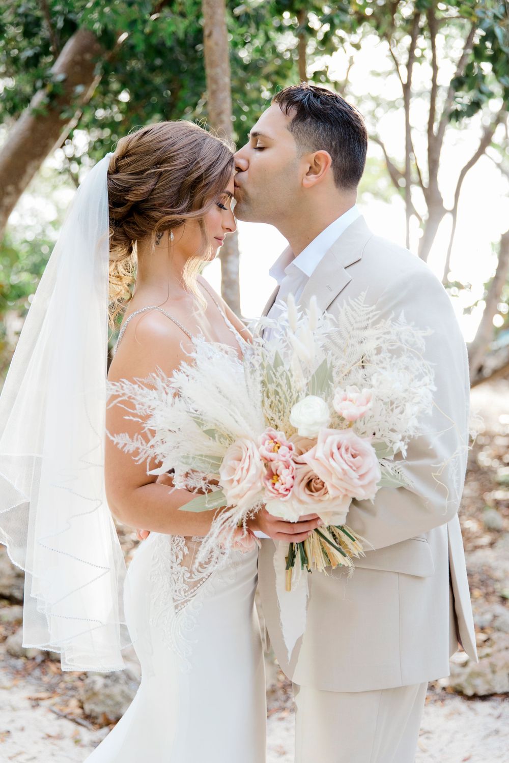 Romantic wedding portrait with bride holding blush and white bouquet in outdoor garden setting.
