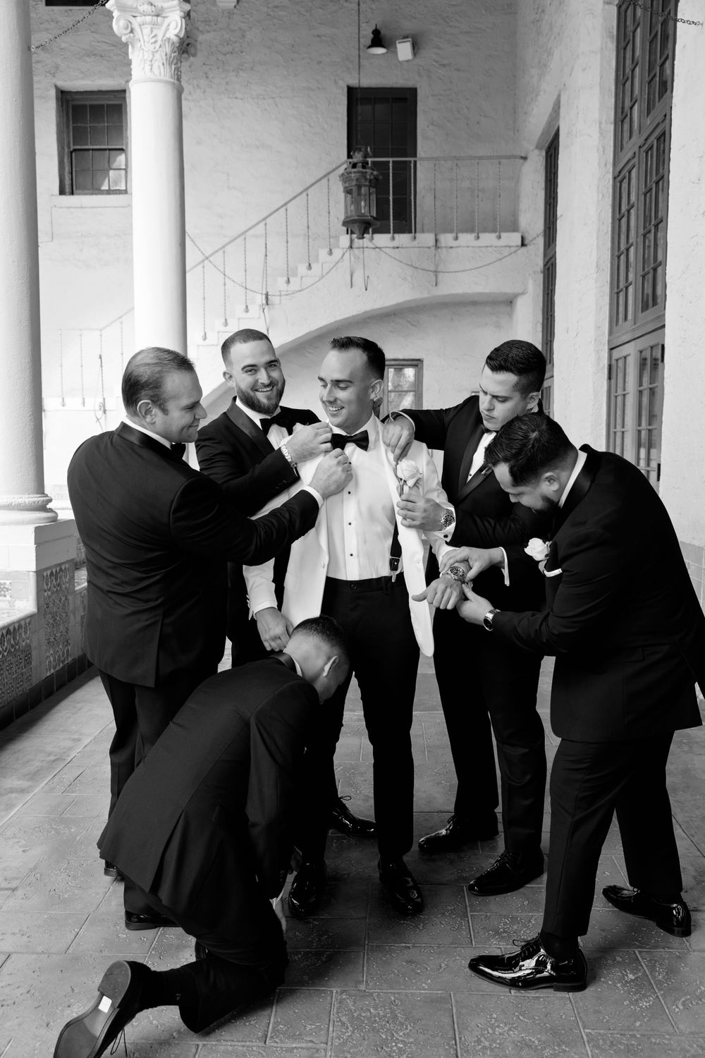 Group of groomsmen helping with wedding preparations in black and white photography.