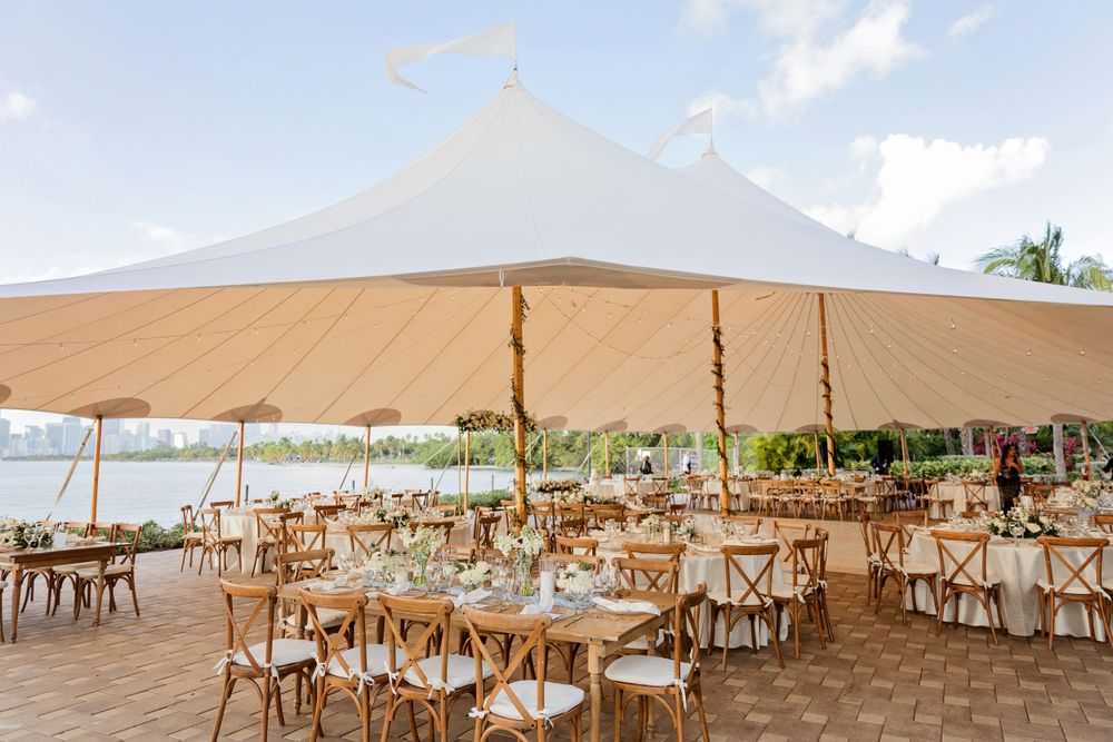 Elegant outdoor beach wedding reception setup with tent and cross-back chairs.