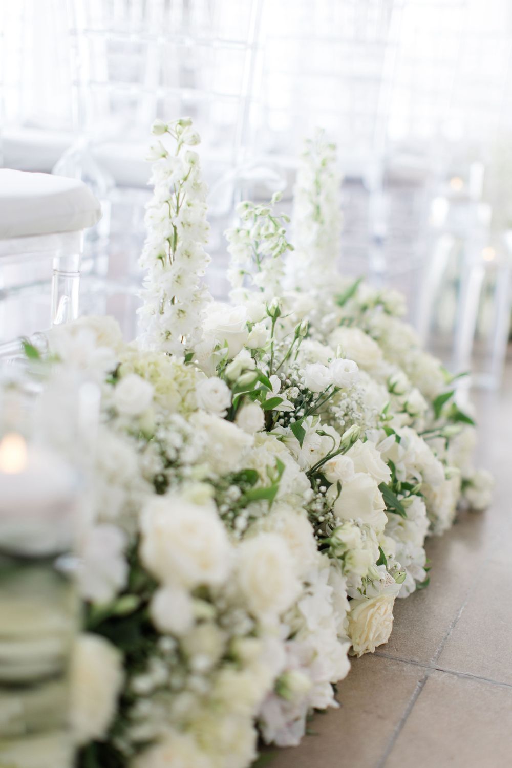 Elegant white floral centerpiece with delicate blooms and greenery on a reception table.