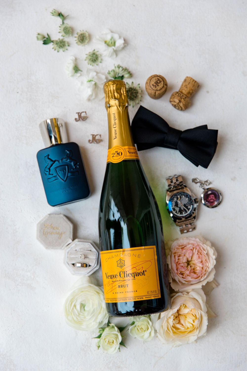 Veuve Clicquot champagne bottle styled with flowers, bow tie, cologne and wedding accessories.