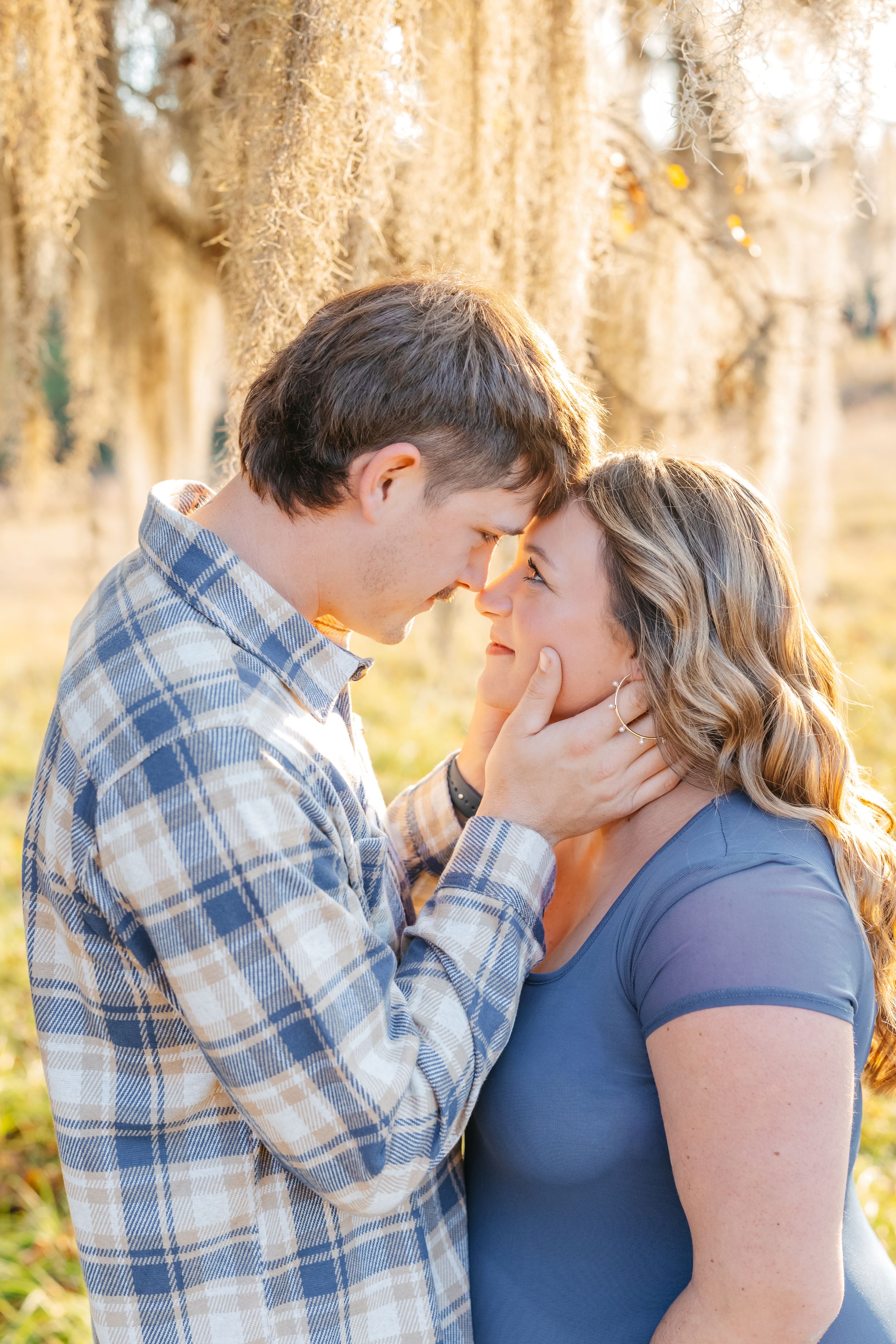 A romantic couple shares intimate moments in a sunlit forest setting wearing blue and plaid clothing.