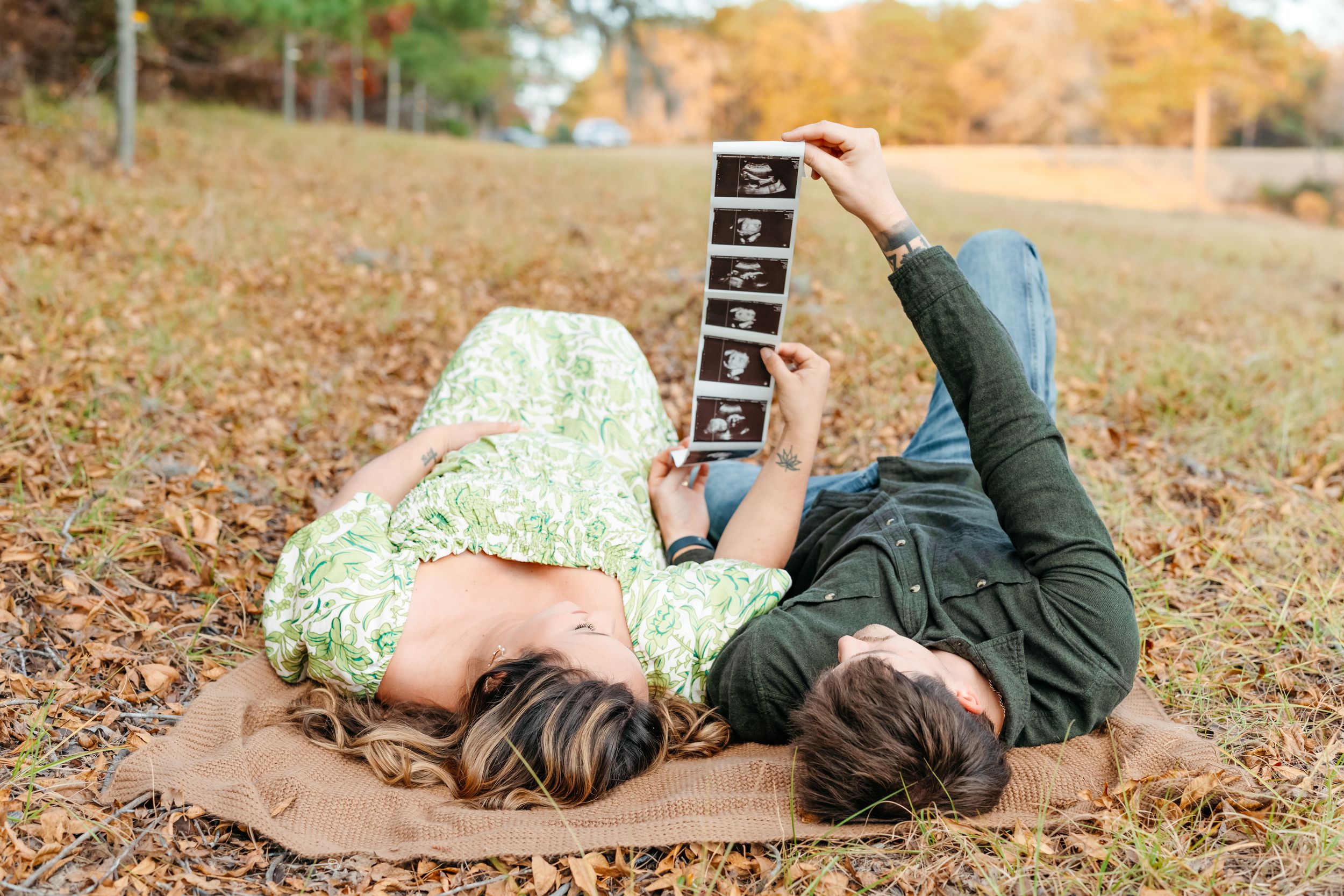 A series of romantic autumn photos showing a couple laying in fallen leaves while looking at a sonogram printout.