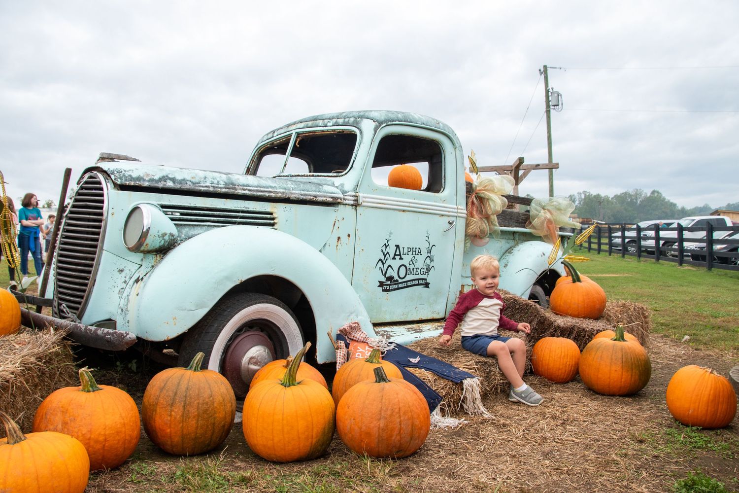 Boy sits in front of the blue truck with pumpkins at Alpha and Omega Corn Maze.
