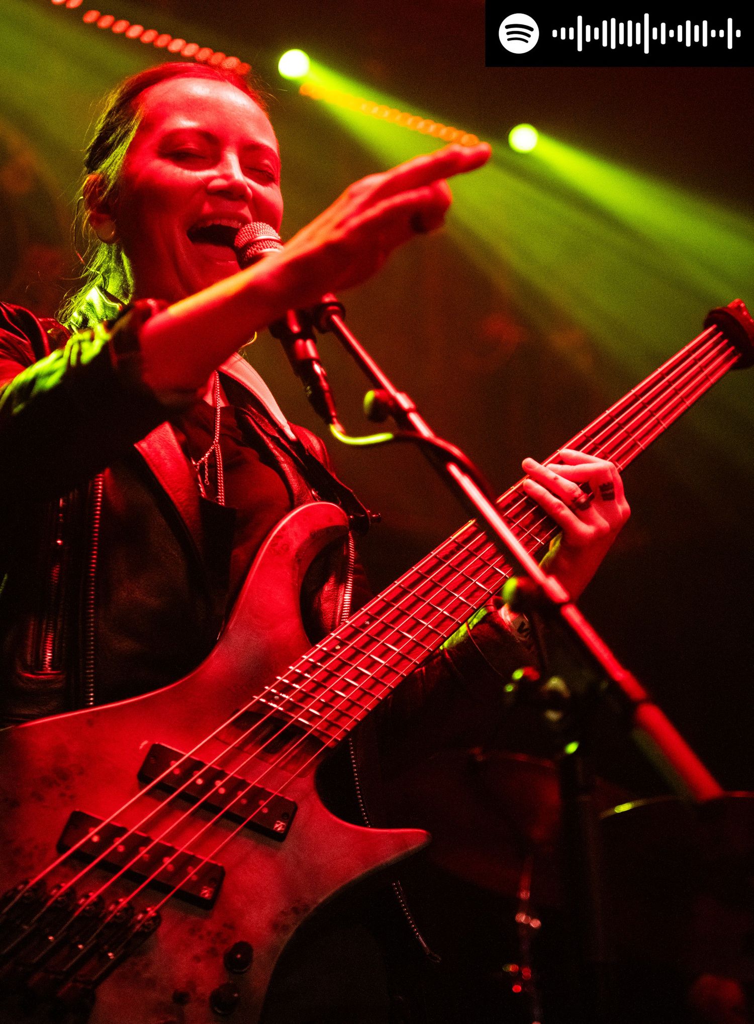 Lindsay holding a bass and singing, reaching out to the audience with spotify code in the top right corner
