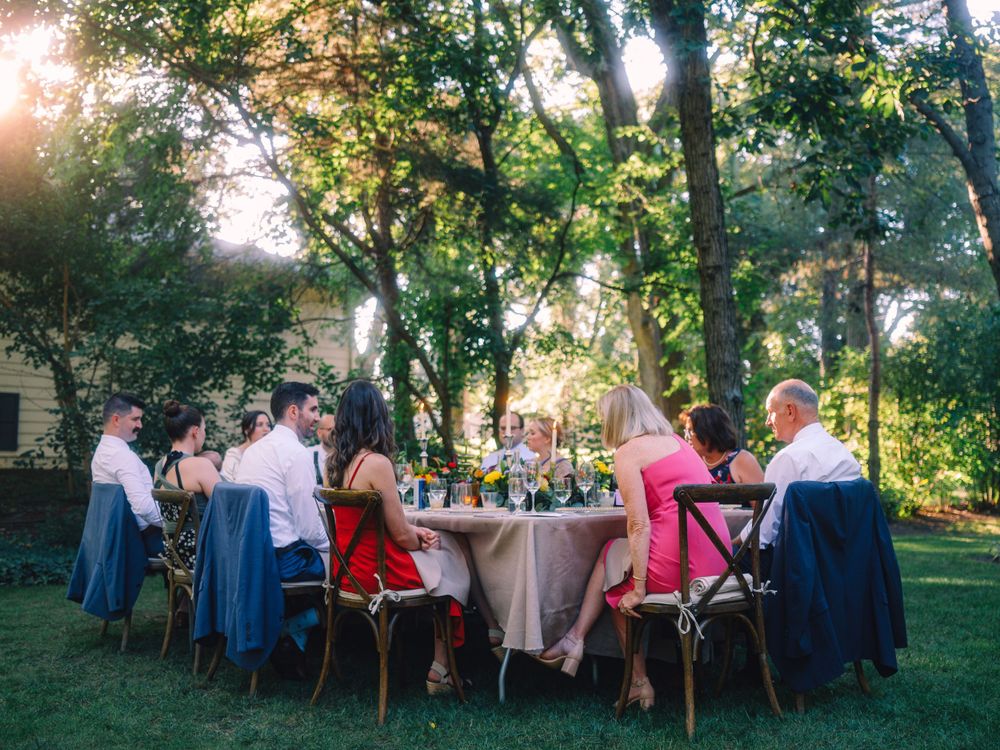 Guests enjoying an elegant outdoor dinner party under tall trees at sunset.