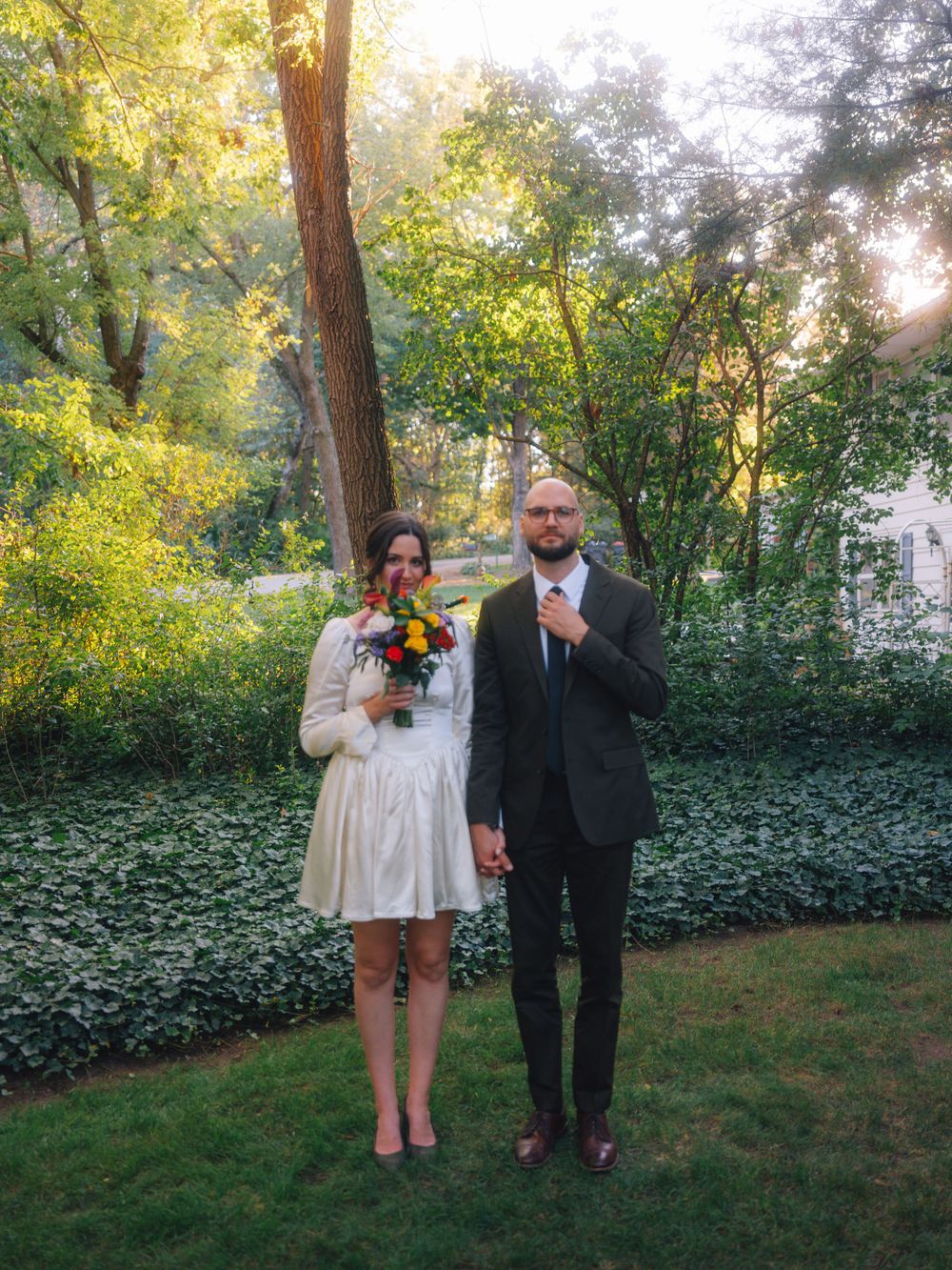 A romantic outdoor wedding photoshoot capturing a couple in a garden with sunlit greenery in the background.