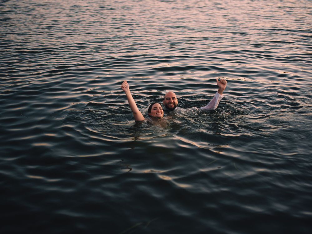 A figure floats with arms raised in sunset-lit water creating ripples across the surface.