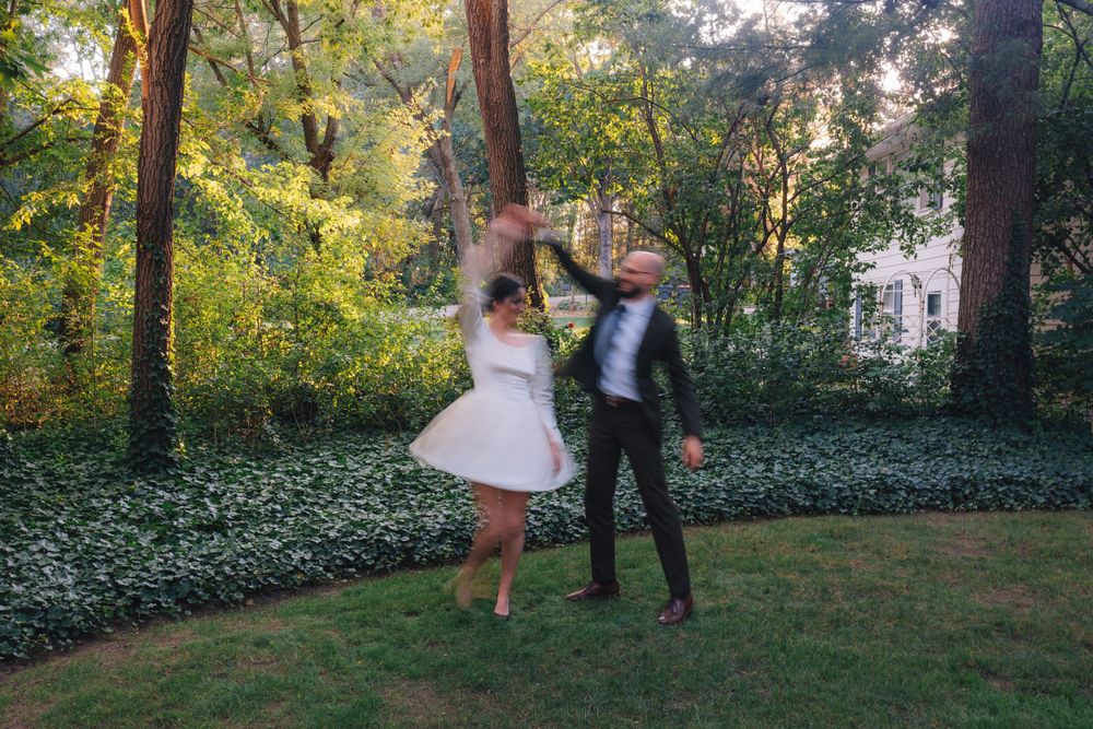 A couple dances playfully in a garden setting with golden sunlight filtering through the trees.