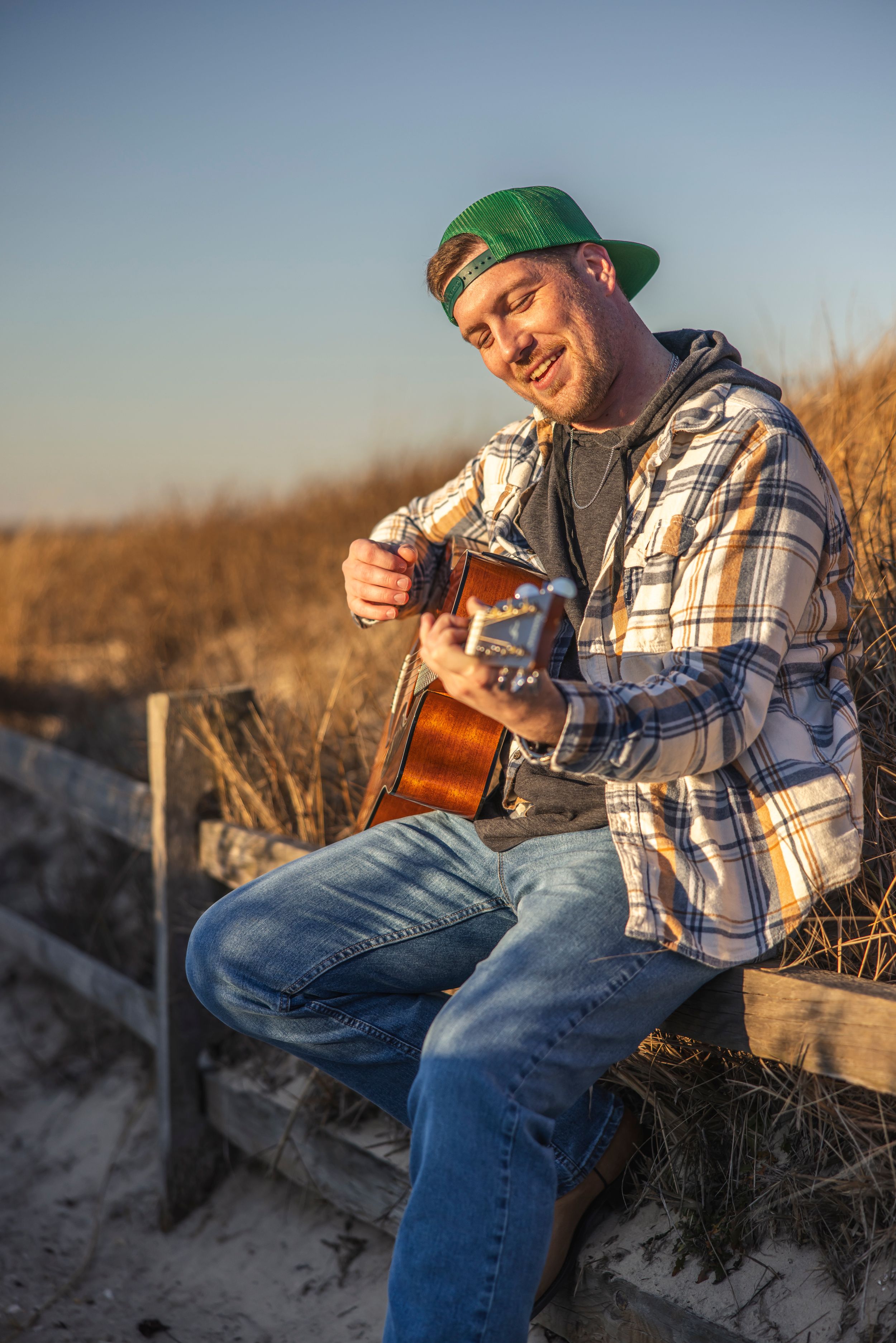 Musician playing acoustic guitar on beach during golden hour sunset.