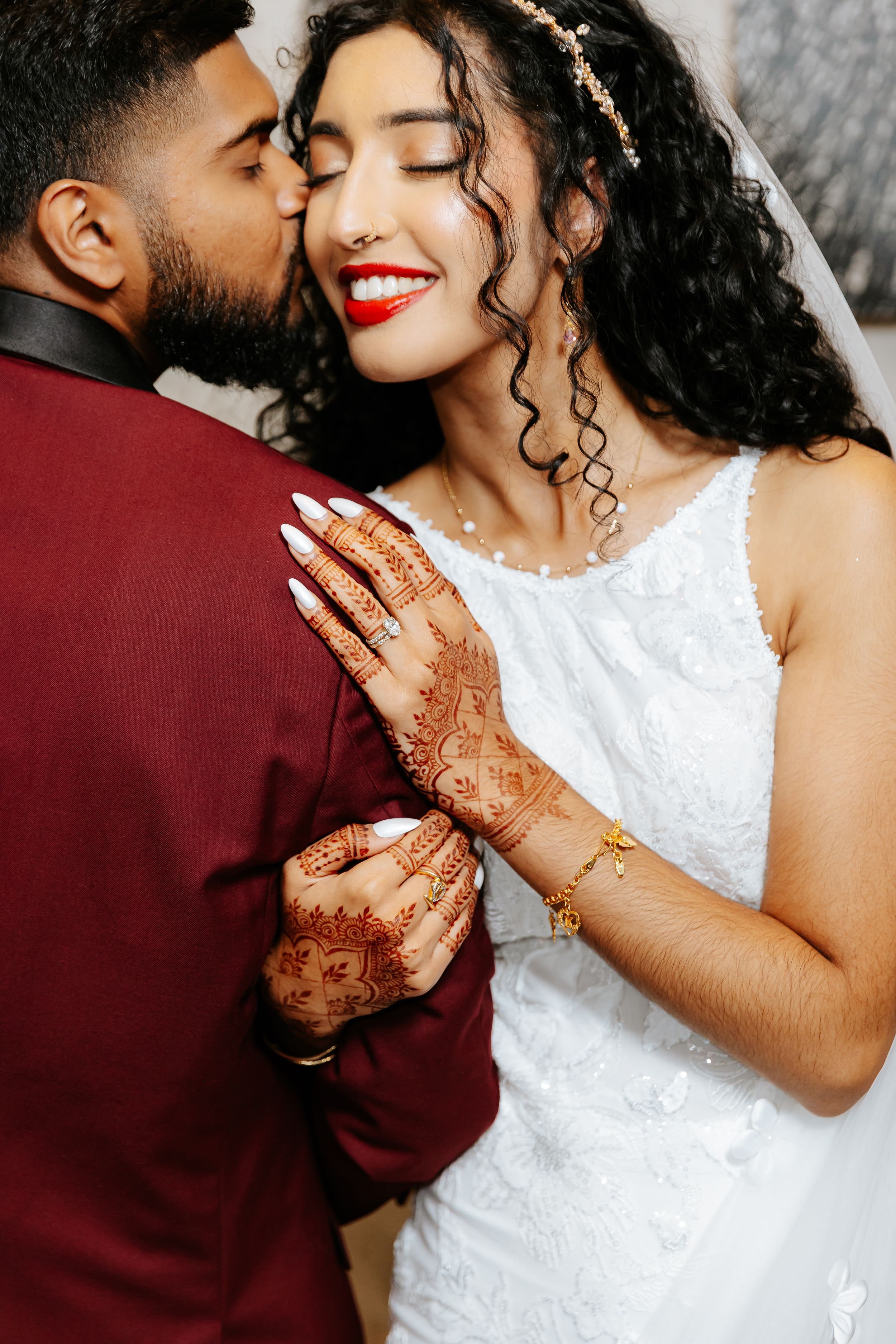 A romantic couple embraces while showing off intricate henna designs and wedding attire.