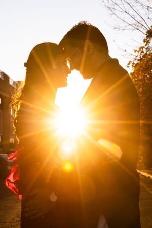 A silhouetted couple embracing in front of a dramatic sunburst during golden hour on an autumn day.