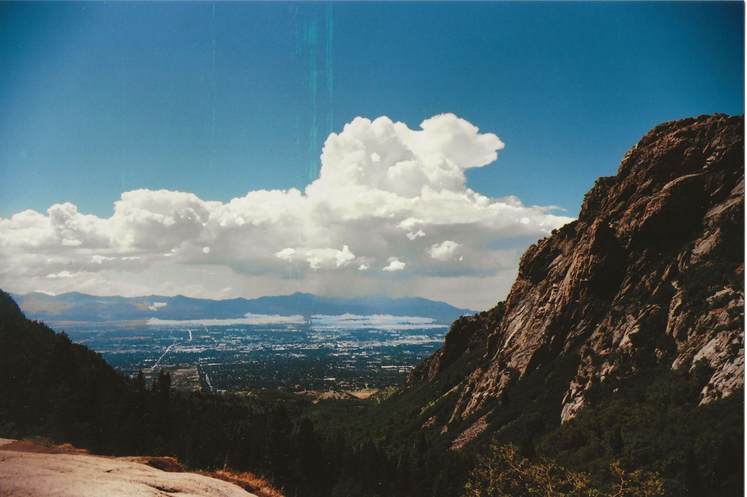 A scenic mountain landscape with dramatic clouds over a distant city valley.