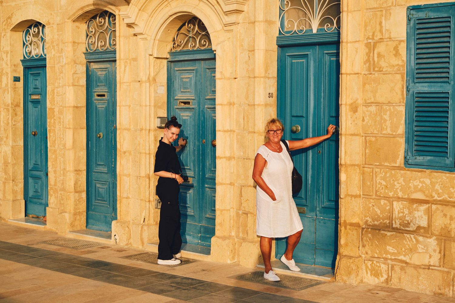 Historic limestone building facade with bright turquoise doors and shutters in Malta.