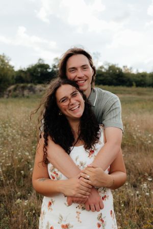 Happy couple embracing in sunny wildflower field during summer.