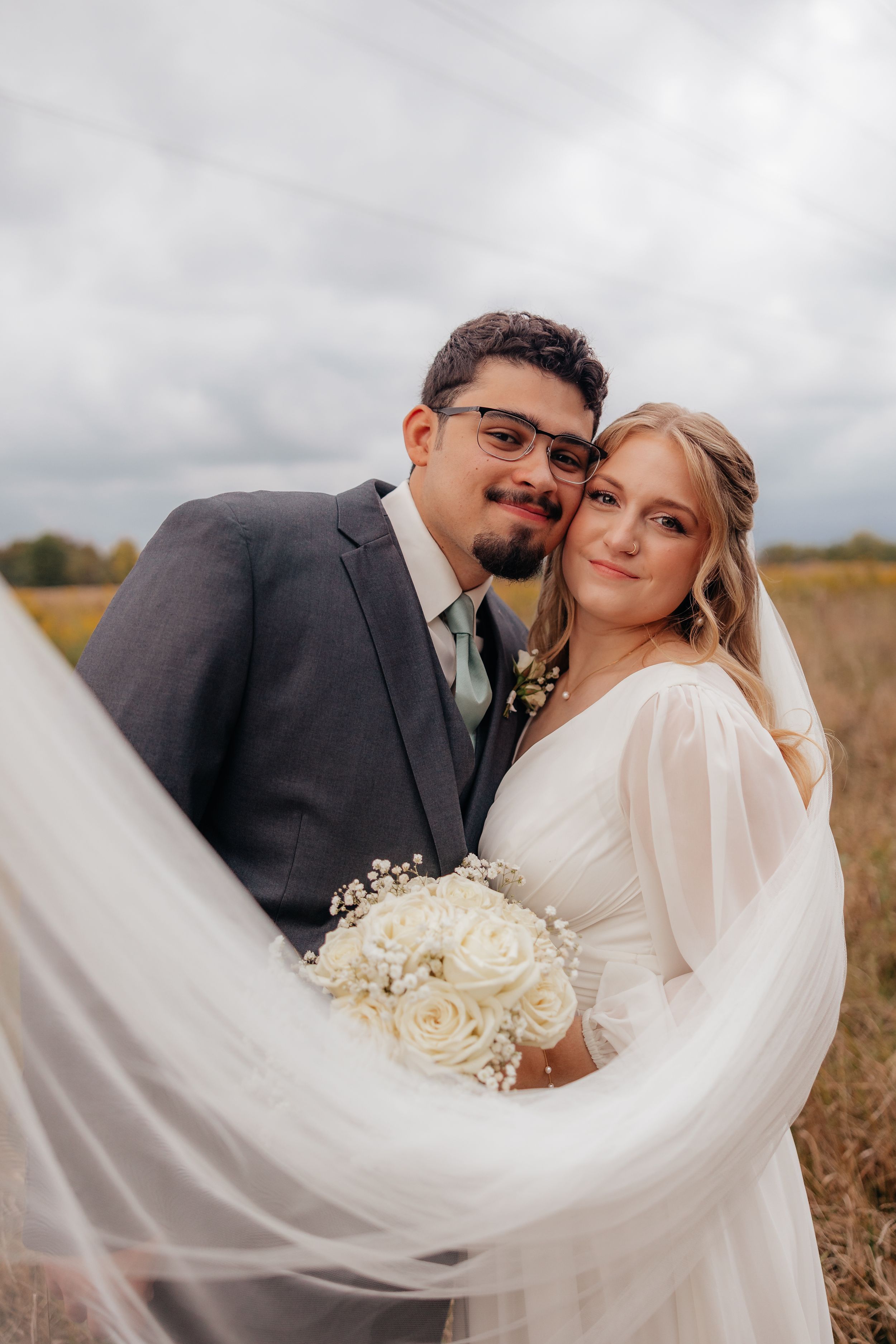 Wedding portrait with flowing veil in rustic field setting.