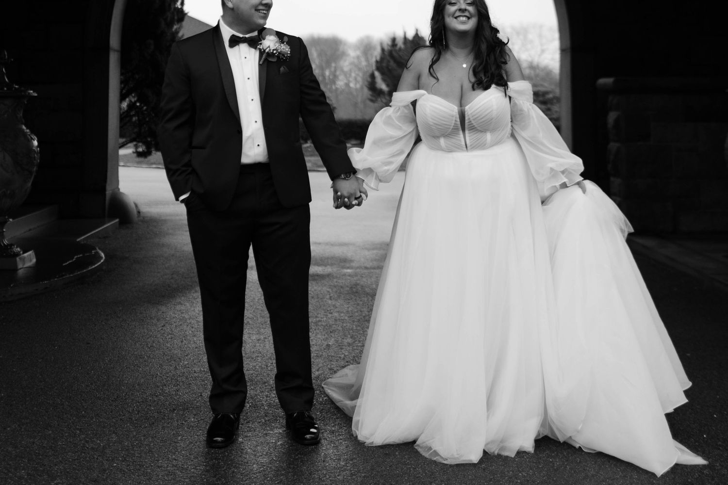 A black and white wedding photo of a bride in a flowing dress walking with their partner in a tuxedo.
