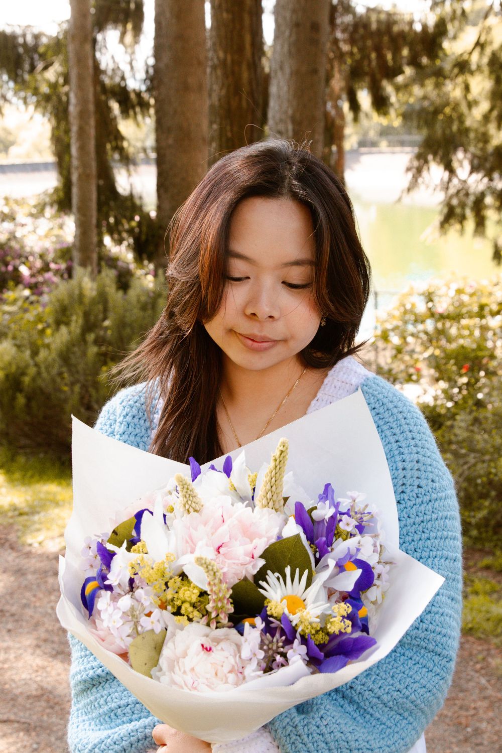 Person holding a vibrant bouquet with pink and purple flowers against an outdoor garden setting.