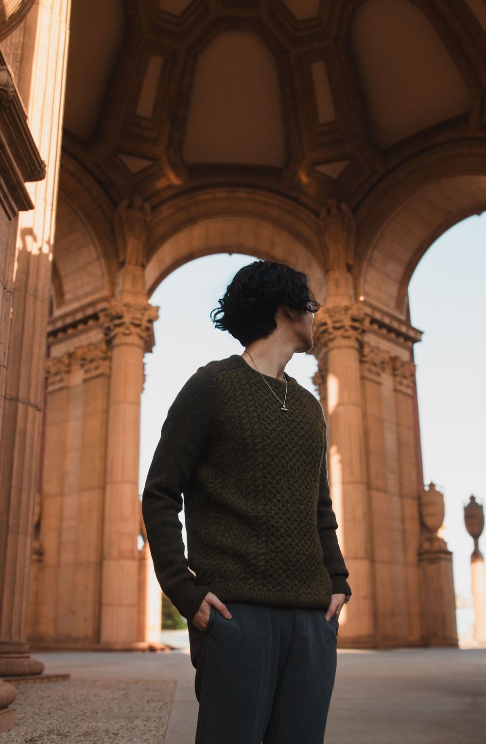 Figure in dark sweater silhouetted against arched architectural columns.