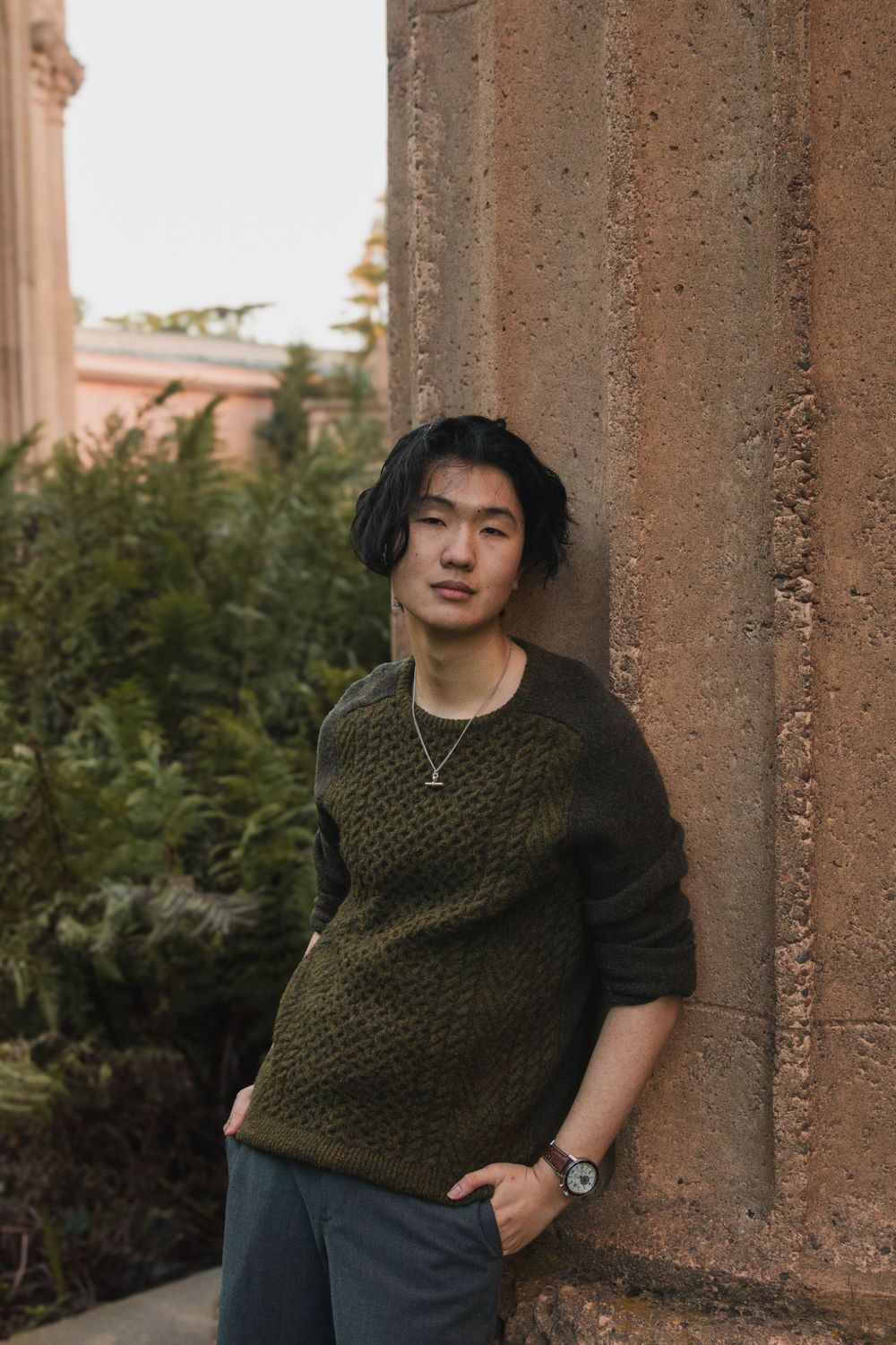 Person in olive knit sweater leaning against stone pillar.