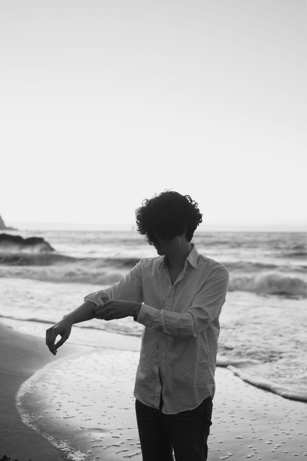 Artistic black and white portrait of person dancing on beach with waves in background.