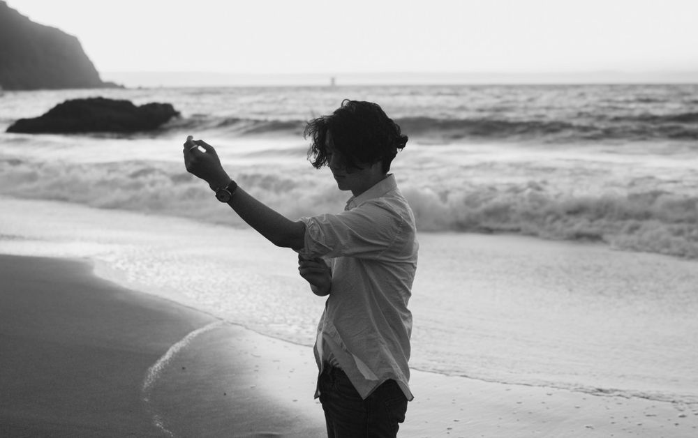 Silhouette of person making expressive gestures against ocean backdrop at sunset.