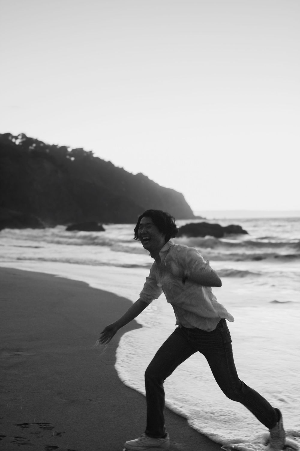Dynamic black and white photo capturing joyful movement on beach with rocky coastline.