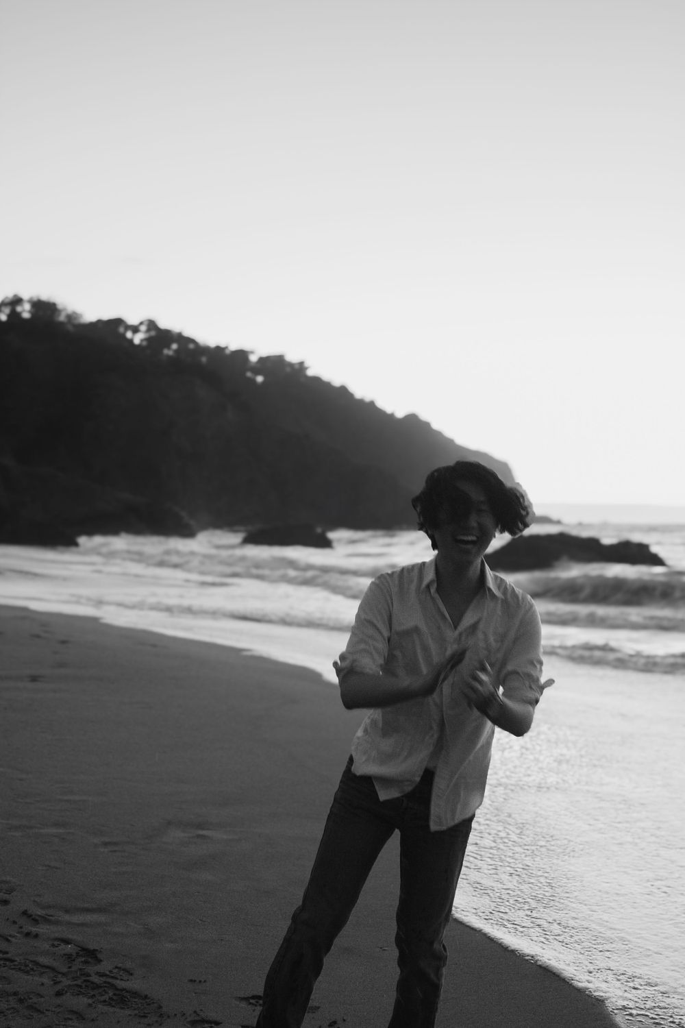 Candid black and white beach portrait showing genuine laughter against coastal backdrop.