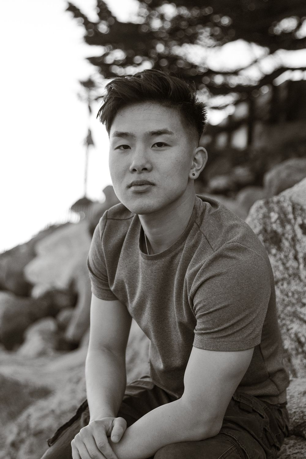 Artistic black and white portrait of a person sitting on rocky terrain.