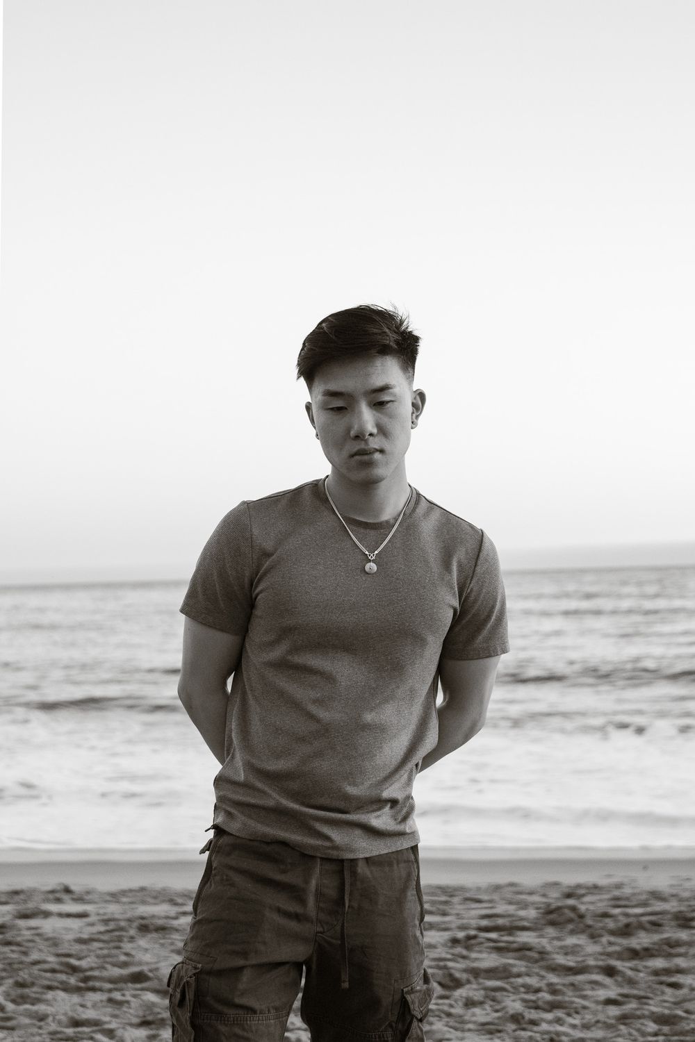 Moody black and white portrait taken at a beach with ocean waves in background.