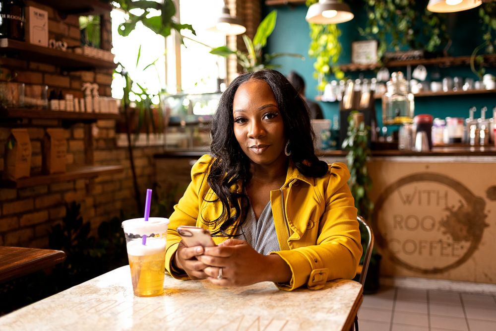 A woman in a yellow jacket sits at a cafe counter with a drink.
