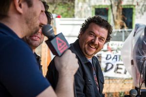 Two people engaged in outdoor interview with microphone against blurred background.
