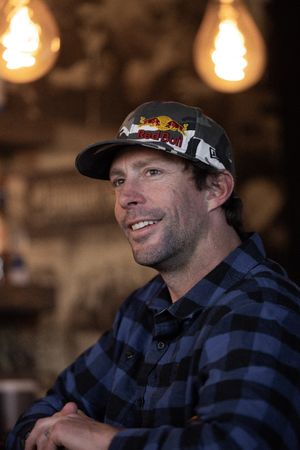 Person in plaid shirt and Red Bull cap smiling at bar under warm lighting.