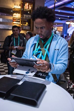 Conference attendee in light blue jacket examines tablet device at networking event.