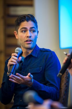 Speaker in navy blue shirt presenting with microphone in professional setting with blue lighting.