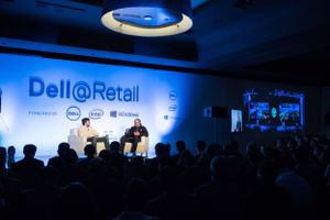 Dell Retail conference stage with speakers and audience silhouetted against blue lighting.