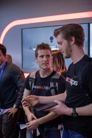 Two staff members in black t-shirts discuss during a tech event with neon lighting in the background.