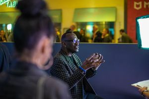 Conference attendee engaged in animated discussion with colleague in darkened room.