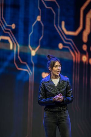 Speaker on stage with futuristic circuit board background design in blue lighting.