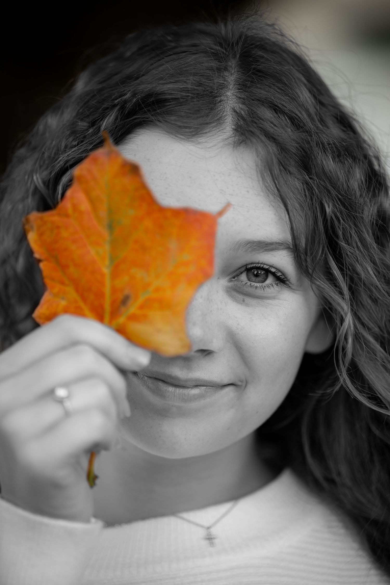Black and white portrait with an orange autumn maple leaf held up to cover part of the face.