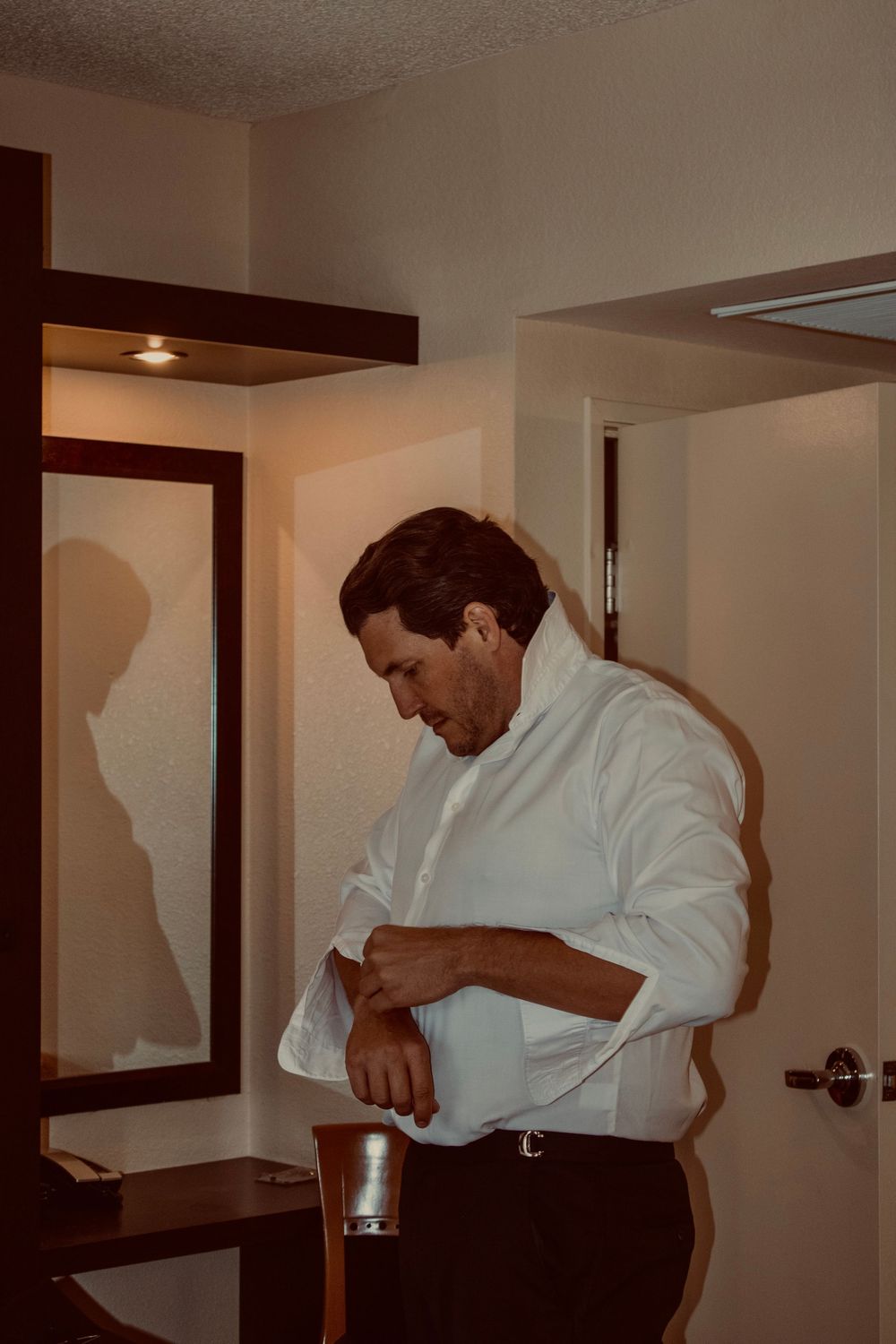 Man in white dress shirt adjusting his cufflinks while getting ready for a formal event.