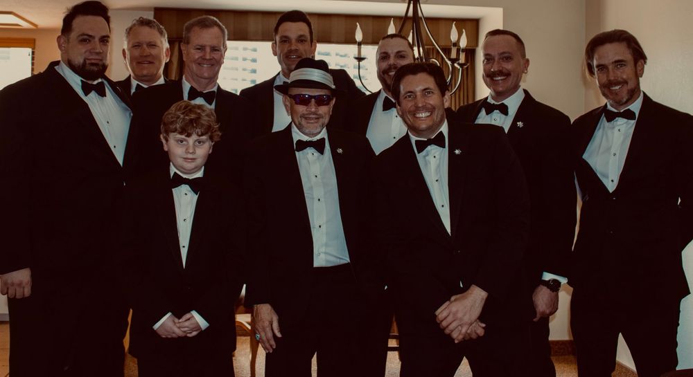 Group of men in black tuxedos posing together at a formal event, smiling for a group photo.