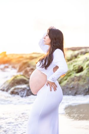 Serene maternity portraits on a sandy beach with dramatic coastal rocks.