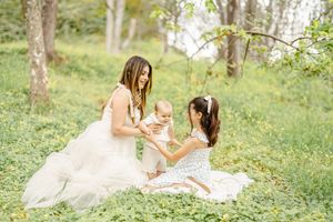Mother and daughter in white dresses sitting together in a sunlit meadow.